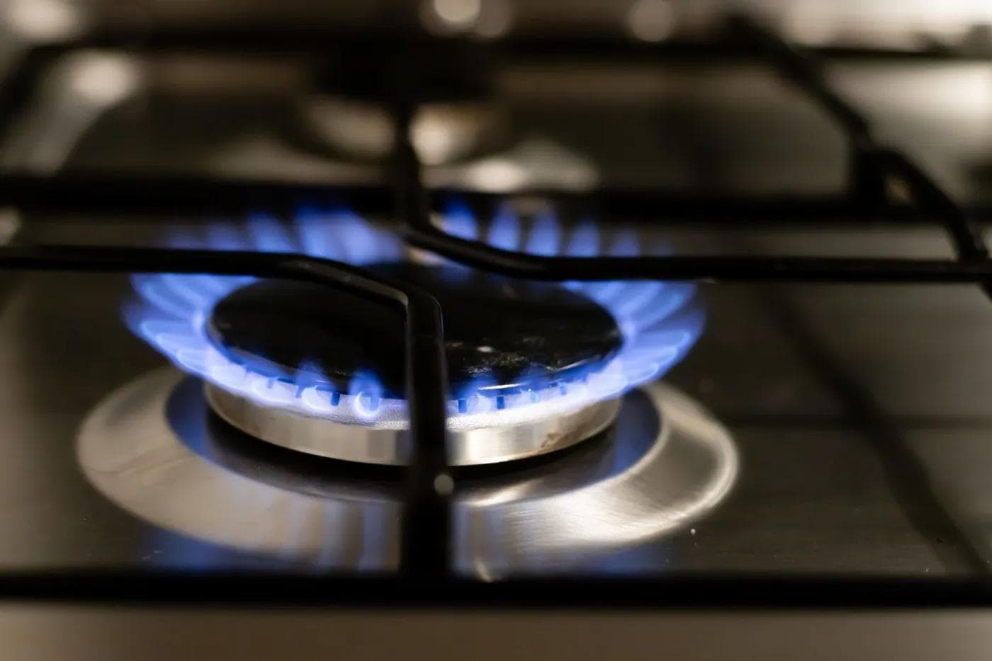 Close-up of a lit gas burner with a blue flame under a cast iron grate